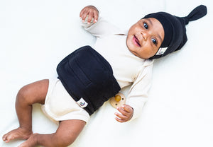 baby on bed wearing noir belly band and top knot hat smiling