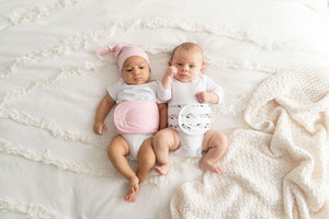 two babies on bed wearing memeeno organic cotton baby belly bands, one in pink and one in feathers print