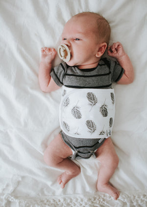 baby on bed wearing plume baby belly band with pacifier in his mouth