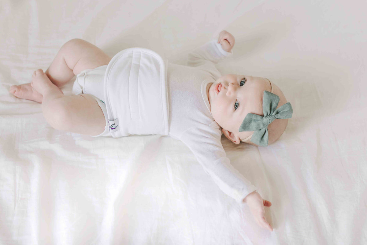  baby lying on bed wearing organic cotton colic, gas, colic remedy white for boy or girl