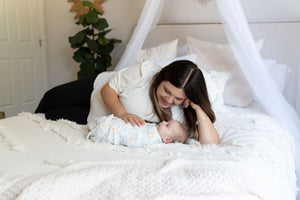 mom and baby on bed with baby swaddled in luna swaddle