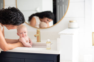 Mom holding a baby on a sink with baby massage oil on the side.