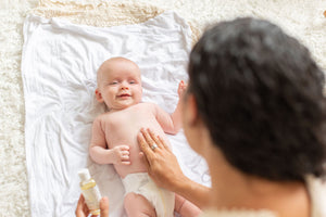 Mom holding baby's tummy and baby massage oil.