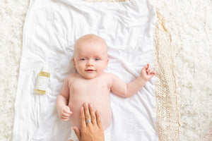 Hand on baby's tummy with a baby massage oil on the side.