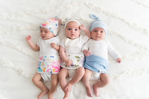 three babies lying on a bed wearing baby belly bands and top knot hats