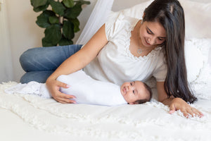 mom and swaddled baby laying in bed